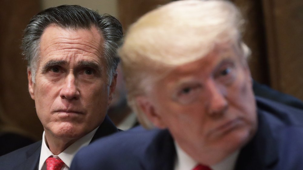 Mitt Romney parece severo sentado detrás de Donald Trump