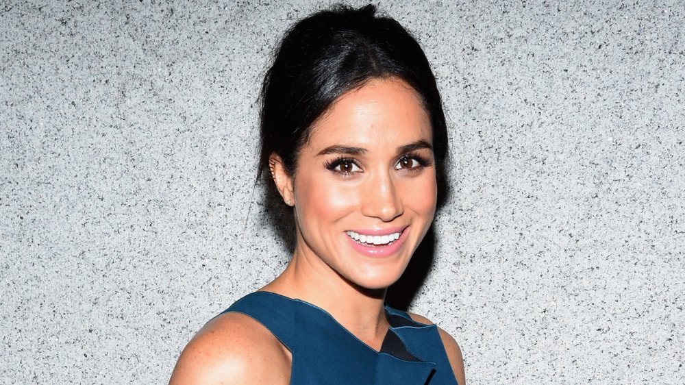 Meghan Markle con un vestido azul, sonriendo a la cámara