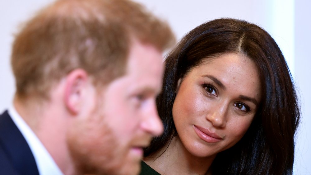 Meghan Markle mirando a Harry, que está fuera de foco.