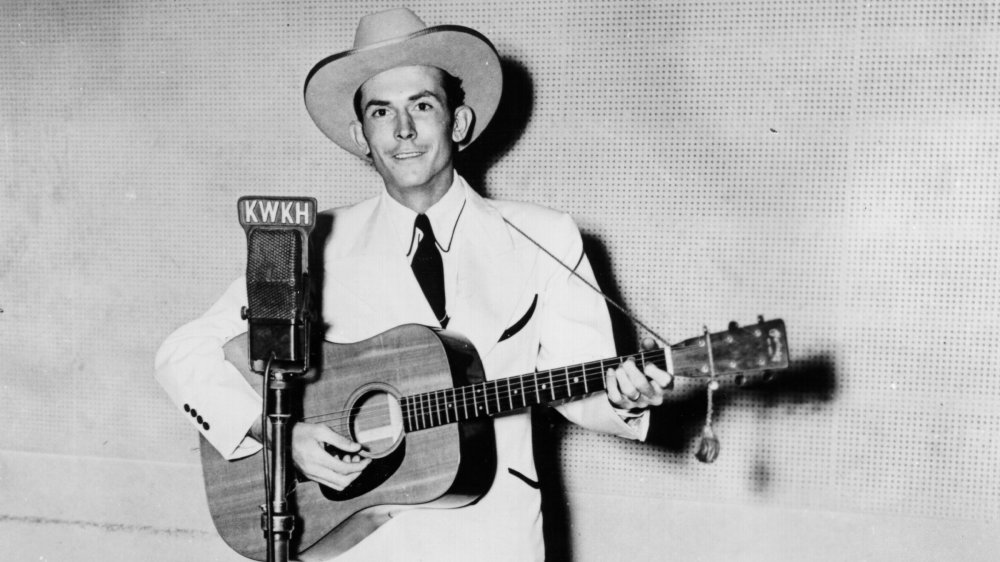 Hank Williams con su guitarra, posando delante del micrófono