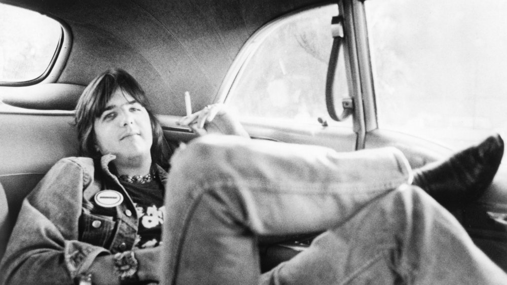 Gram Parsons recostado en un automóvil, fumando un cigarrillo