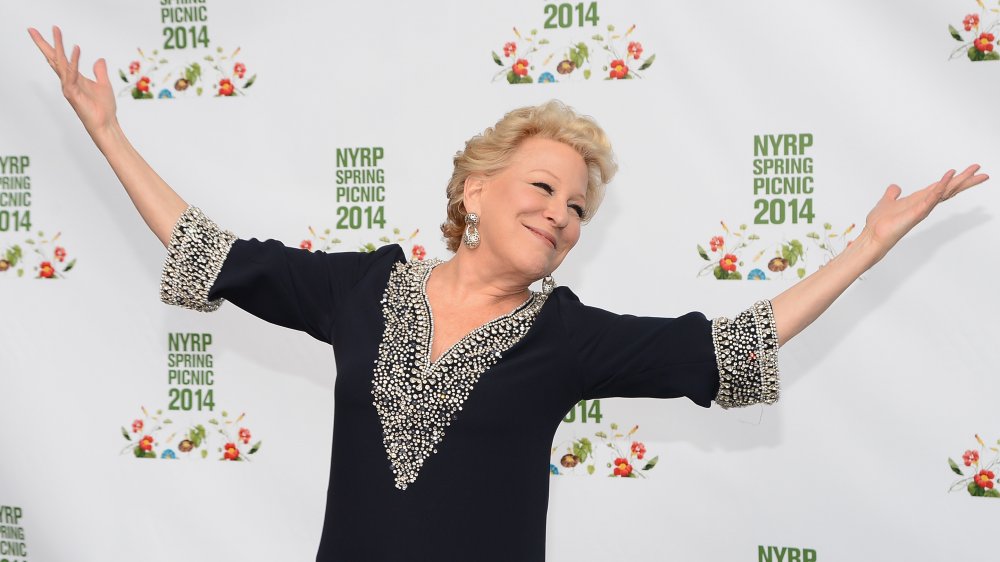 Bette Midler sonriendo con las manos en alto sobre la alfombra roja