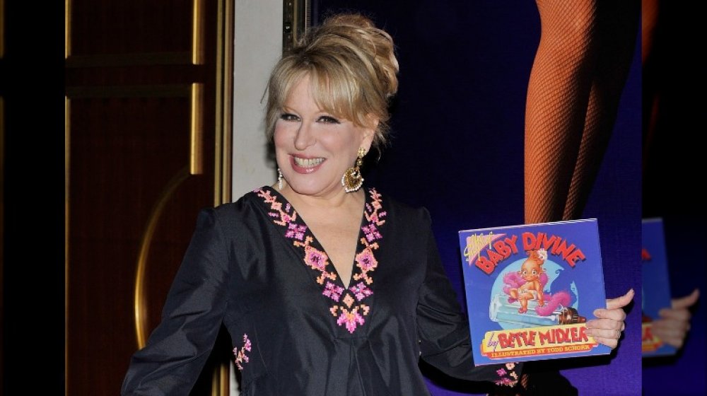 Bette Midler sonriendo mientras sostiene su libro Baby Divine