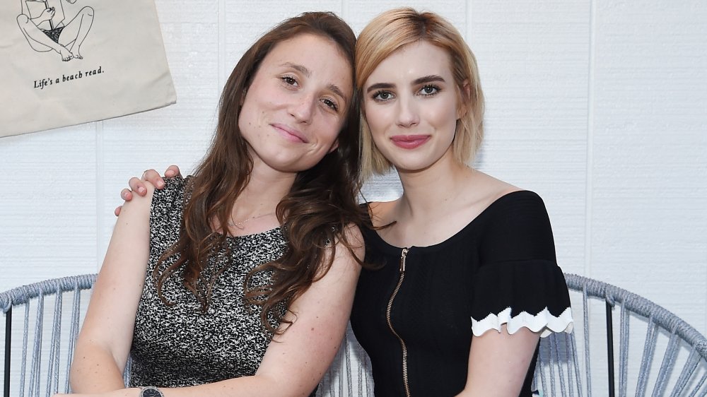 Karah Preiss y Emma Roberts sentadas juntas con pequeñas sonrisas