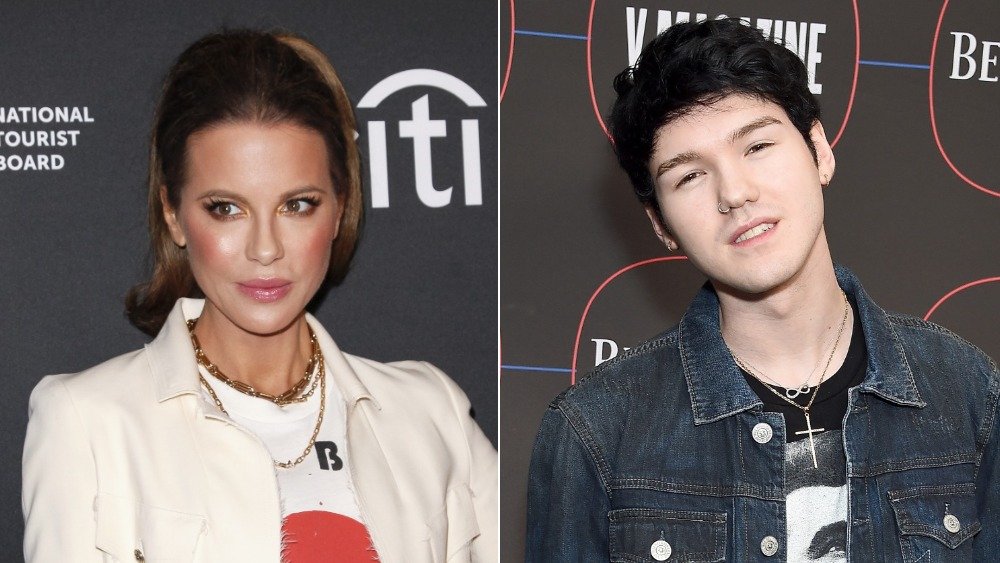 Kate Beckinsale con un top blanco y un blazer y Goody Grace sonriendo a la cámara con la cabeza ladeada