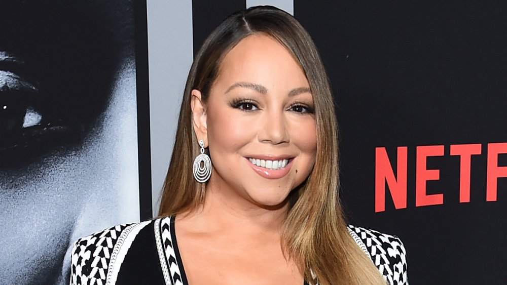 Mariah Carey sonriendo frente al muro promocional de Netflix