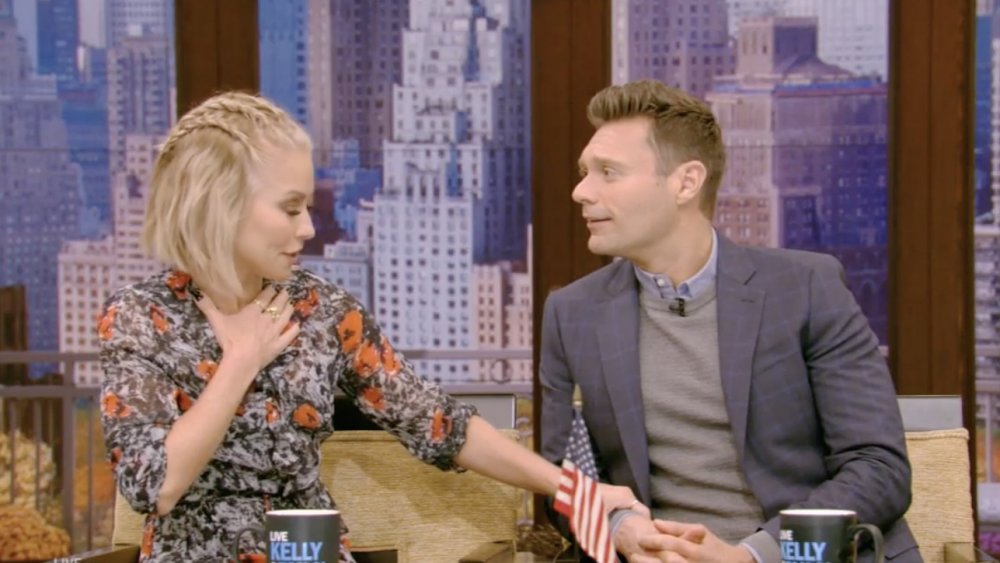 Kelly Ripa agarrando la mano de Ryan Seacrest en el aire