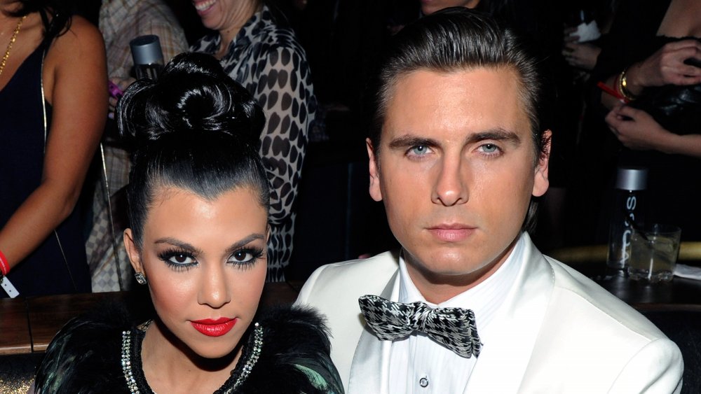 Kourtney Kardashian con labios rojos y moño alto, junto a Scott Disick