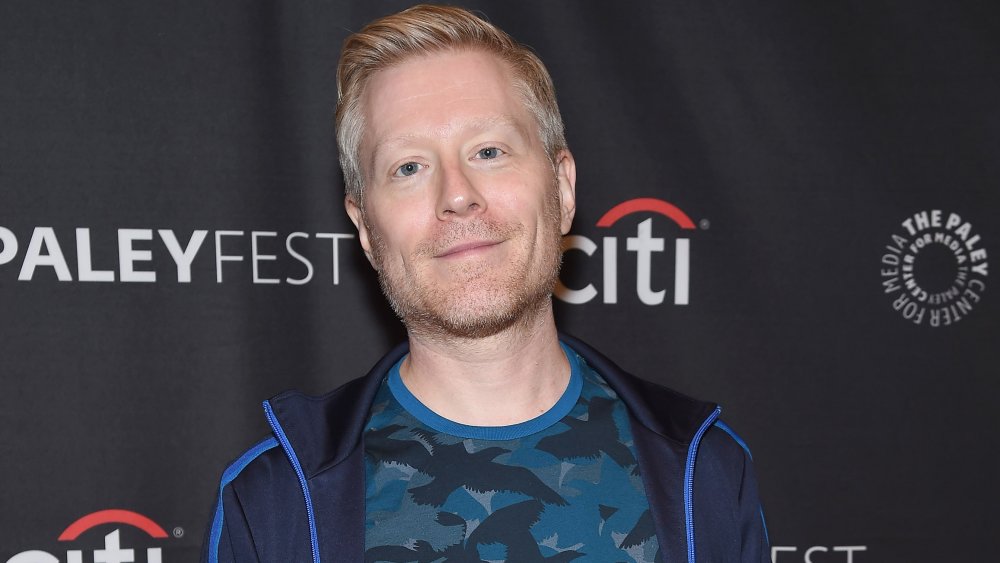 Anthony Rapp sonriendo a la cámara con un traje azul