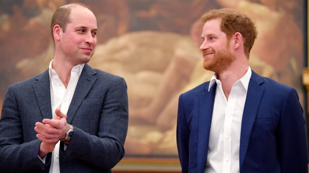 Príncipe William aplaudiendo y mirando al Príncipe Harry, ambos sonriendo.