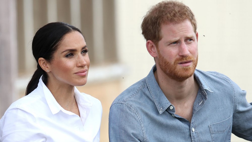 Meghan Markle, el príncipe Harry, ambos vestidos con camisas con botones, se ven serios