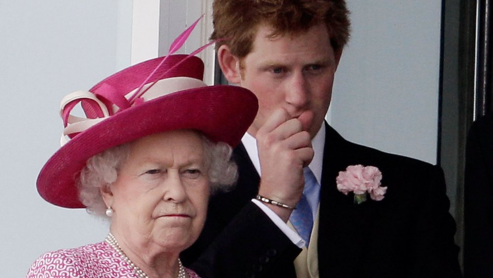 La reina Isabel en una combinación rosa de sombrero y vestido, con aspecto serio frente a un joven príncipe Harry