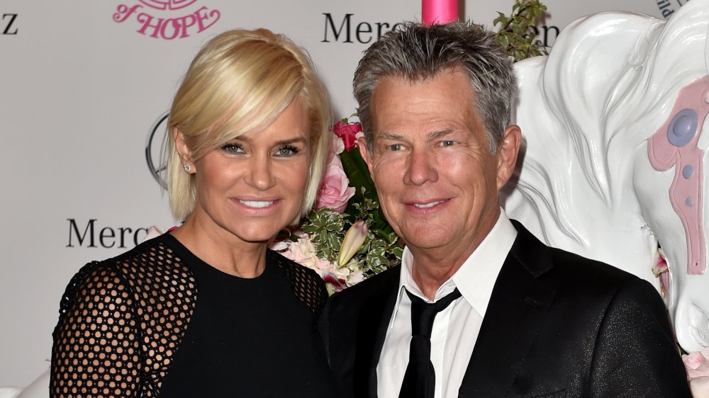 Yolanda Hadid con un vestido de encaje negro, David Foster con un traje negro con corbata negra suelta, sonriendo juntos en un evento