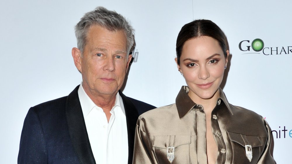 David Foster con un blazer azul oscuro, Katharine McPhee con un jersey dorado brillante, posando juntos en un evento