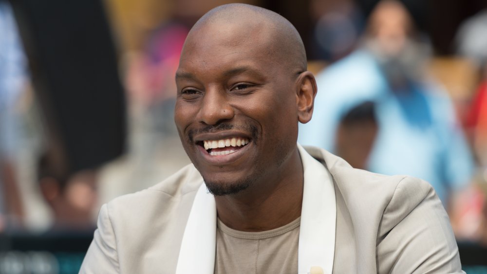 Tyrese Gibson vistiendo un blazer beige y una camisa, sonriendo a lo grande en un evento