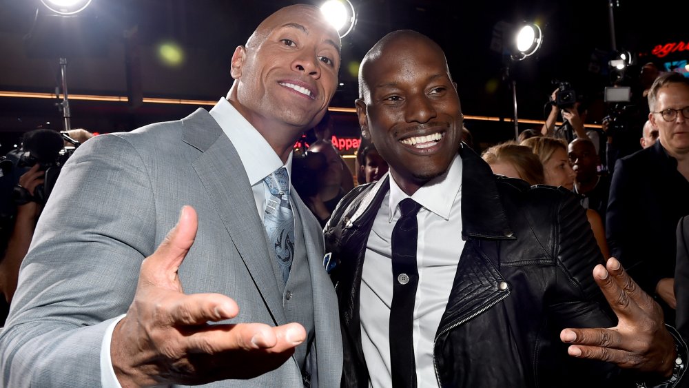 Dwayne Johnson con un traje gris de tres piezas, Tyrese Gibson con una chaqueta de cuero negra, sonriendo juntos en el estreno de una película