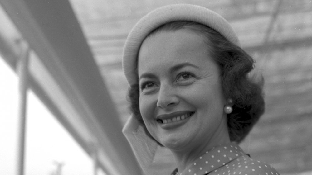 Foto en blanco y negro de Olivia de Havilland con un sombrero y aretes de perlas, sonriendo