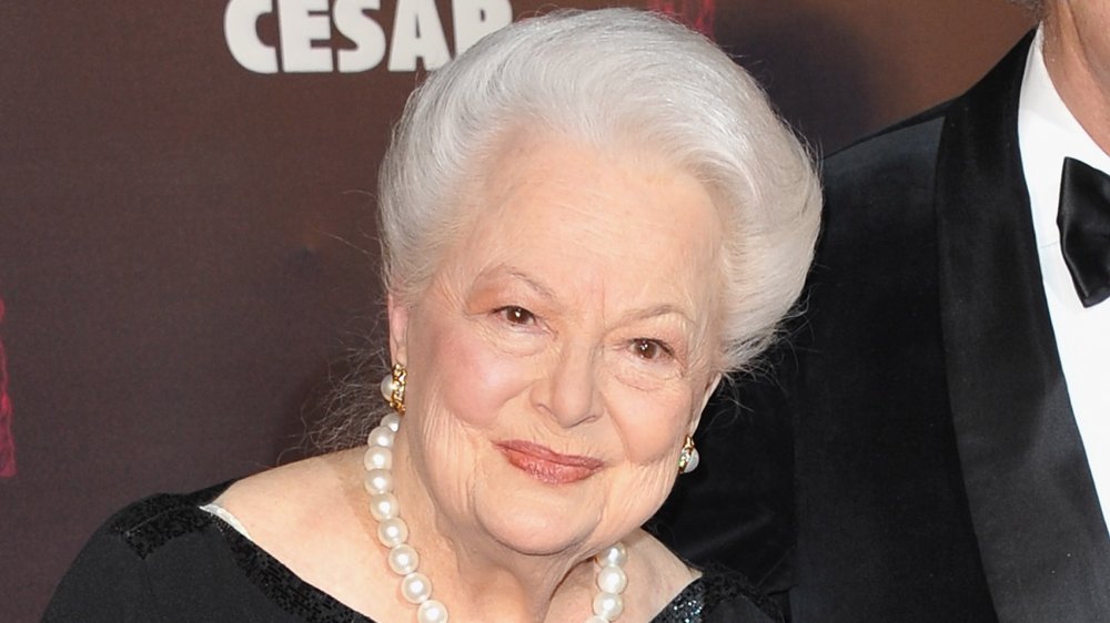 Olivia de Havilland con un vestido negro y perlas, con una pequeña sonrisa en un evento de alfombra roja