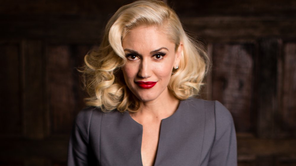 Gwen Stefani con un traje gris y lápiz labial rojo, posando con una pequeña sonrisa