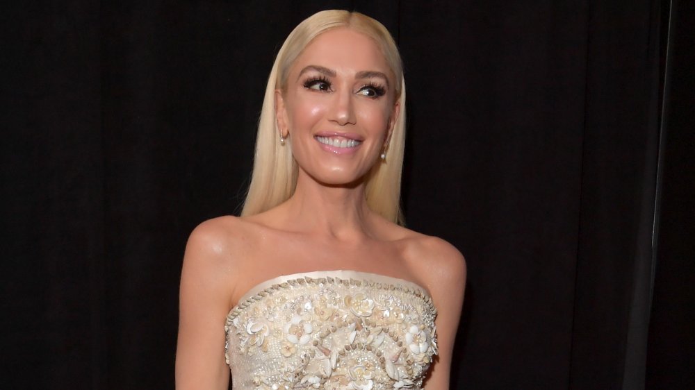 Gwen Stefani con un vestido blanco adornado con joyas, sonriendo mientras mira a un lado