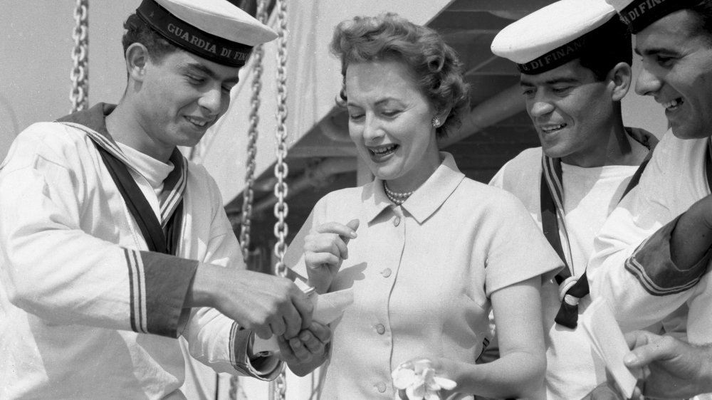 Foto en blanco y negro de Olivia de Havilland sonriendo, rodeada de marineros en 1953