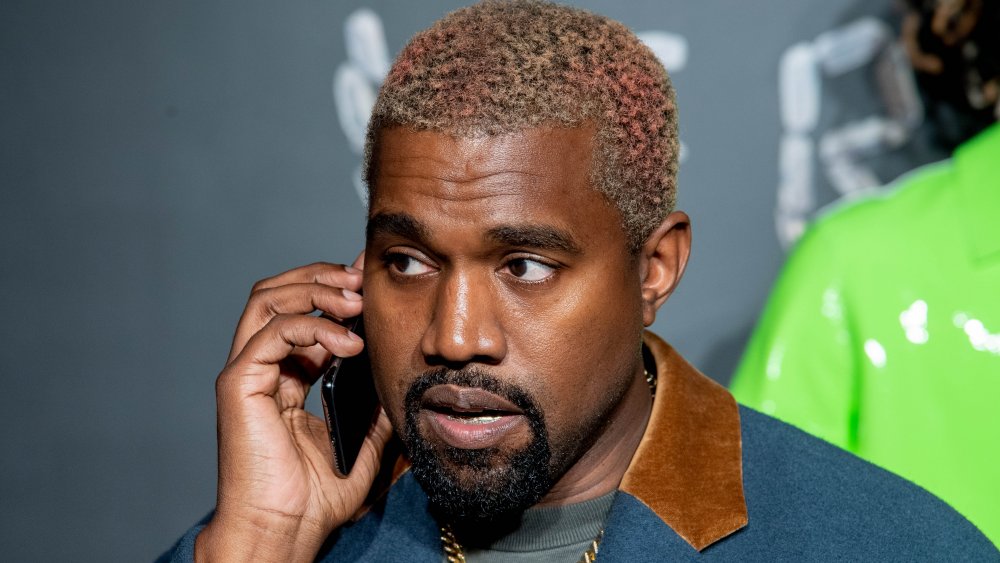 Kanye West con una chaqueta azul y marrón, hablando por teléfono