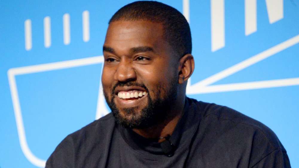 Kanye West con una camisa azul oscuro, sonriendo grande durante una entrevista