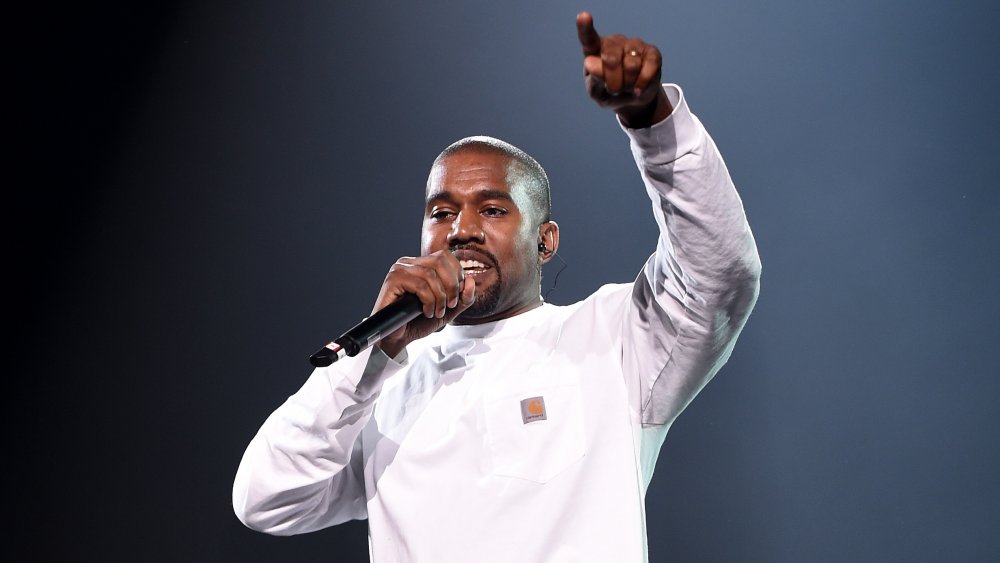 Kanye West con una camisa blanca de manga larga, actuando durante un concierto