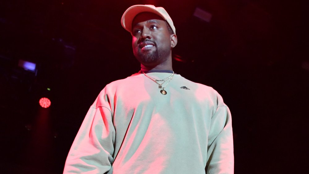 Kanye West con una sudadera blanca y gorra de béisbol, mirando a la multitud durante un concierto