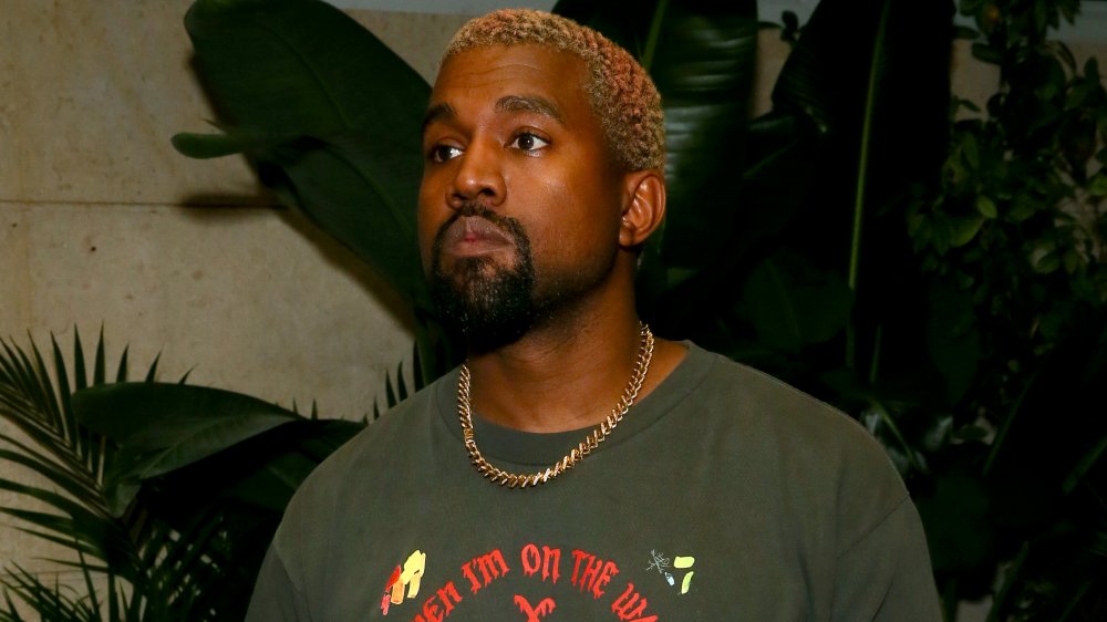 Kanye West con una camiseta estampada gris y una cadena dorada, mirando a un lado con una expresión seria