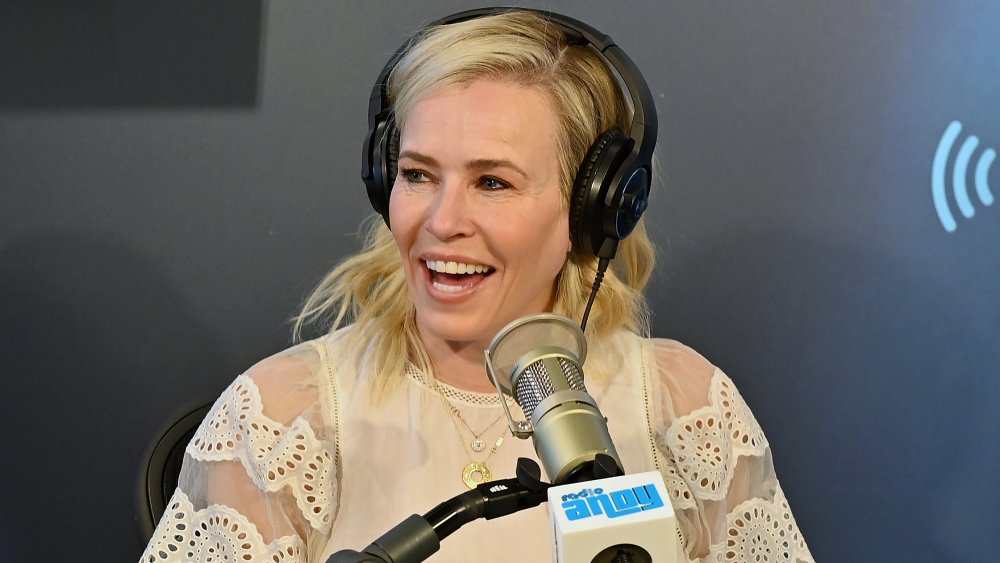 Chelsea Handler con una blusa blanca y auriculares, riéndose del show Sirius XM de Andy Cohen