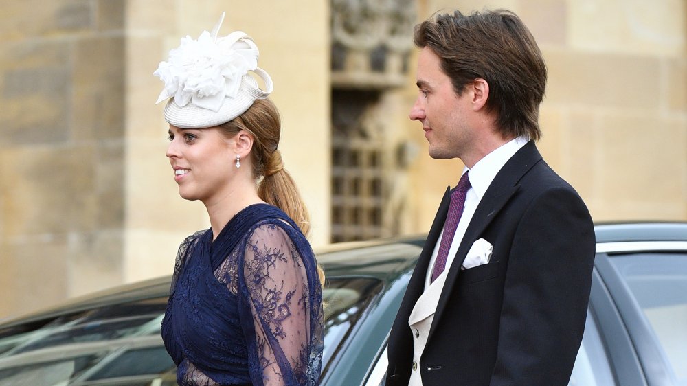 La princesa Beatriz con un vestido azul y un sombrero blanco, caminando mientras Edoardo Mapelli Mozzi observa