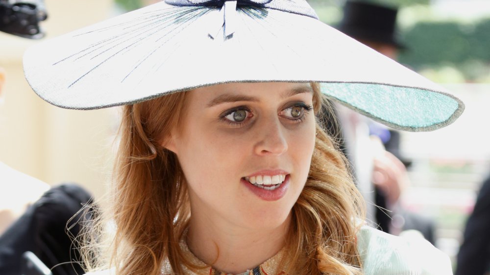 La princesa Beatriz con un traje blanco y un sombrero grande, mirando hacia un lado mientras sonríe