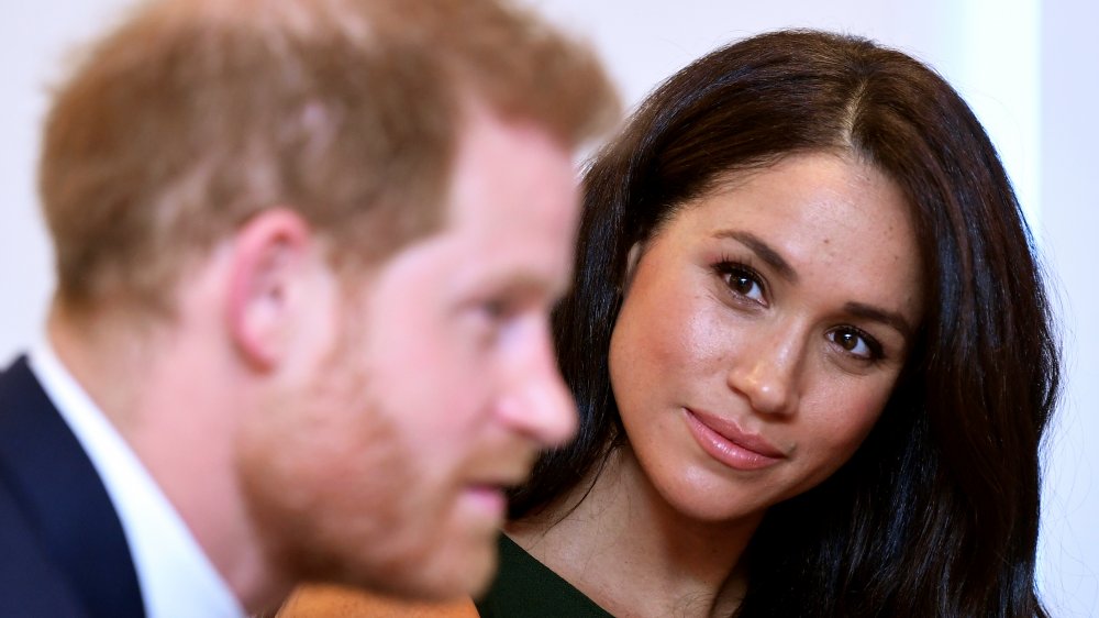 Príncipe Harry hablando con Meghan Markle detrás de él