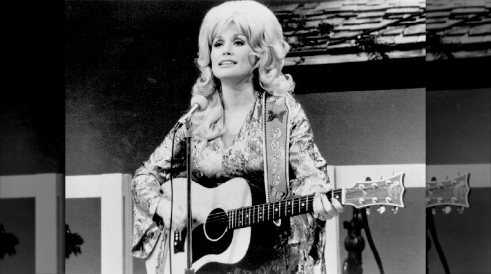 Fotografía en blanco y negro de Dolly Parton cantando y tocando la guitarra en 1974 a los 28 años