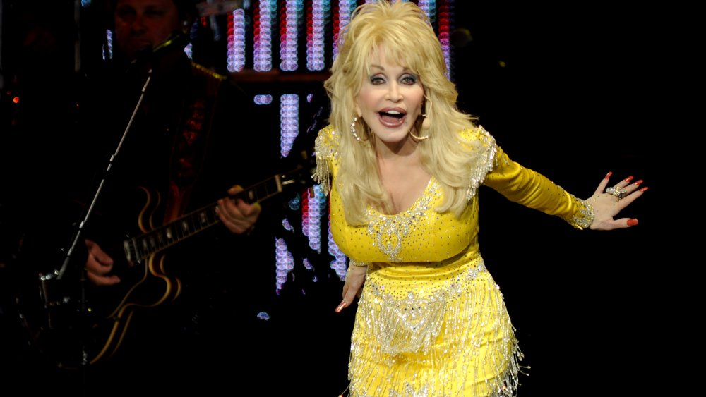 Dolly Parton con un vestido amarillo brillante, en el escenario en 2011 a los 65 años