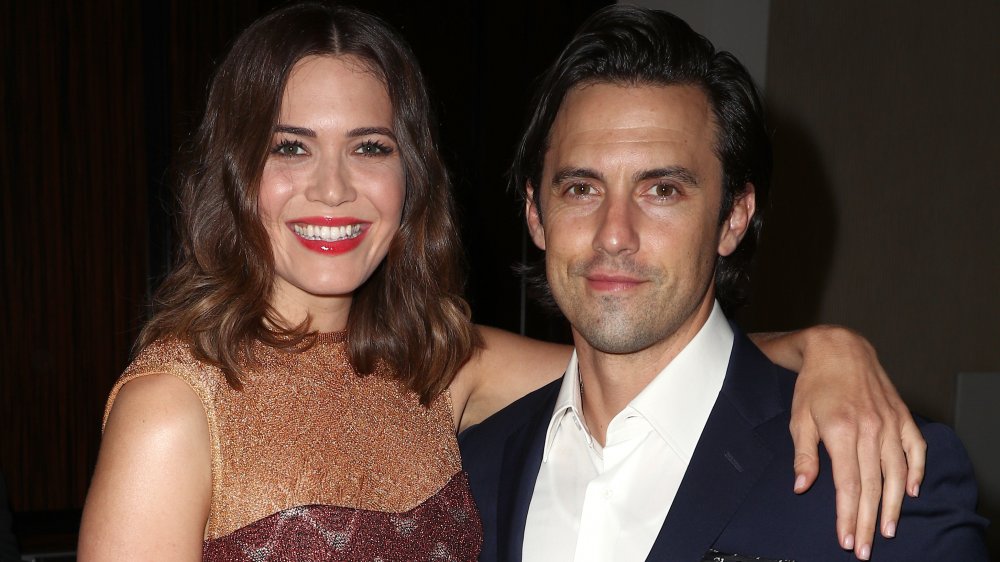 Mandy Moore sonriendo con su brazo alrededor de un sonriente Milo Ventimiglia