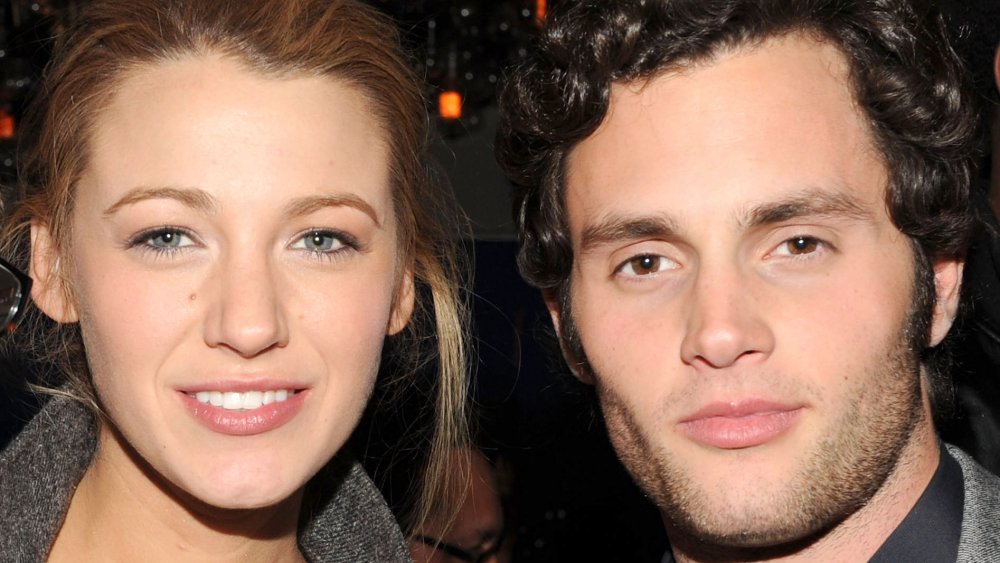 Blake Lively y Penn Badgley, ambos con atuendos grises con pequeñas sonrisas