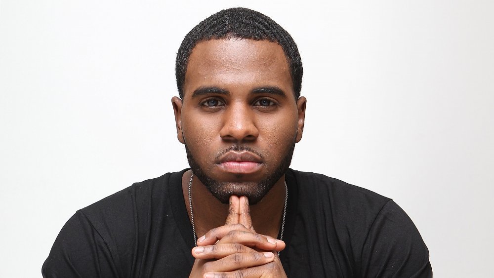 Jason Derulo en una camiseta negra y cadena de plata, posando con una expresión neutra