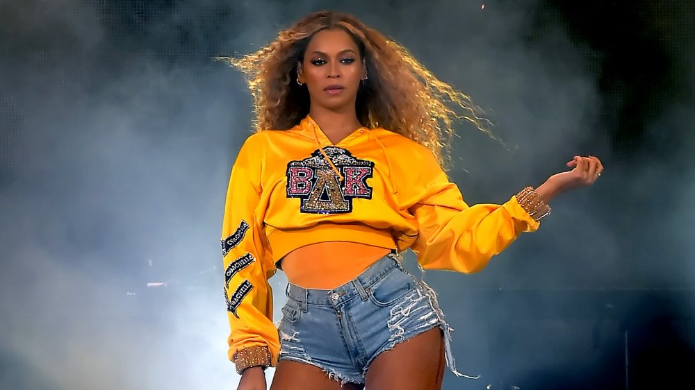 Beyoncé con sudadera amarilla con capucha y pantalones cortos de jean, actuando en Coachella 2018