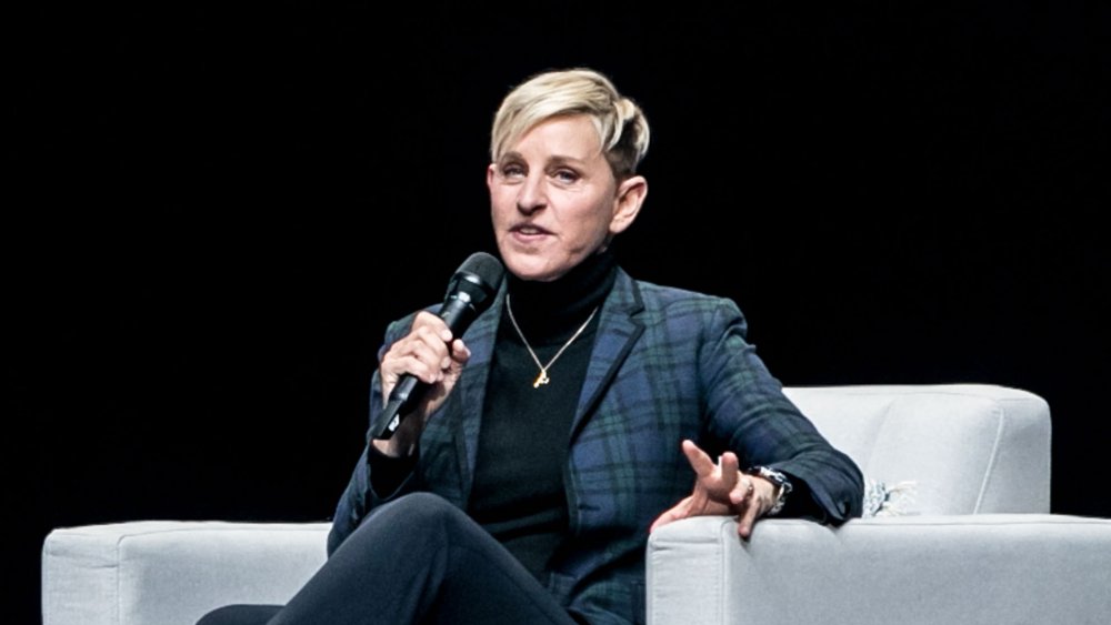 Ellen DeGeneres en un traje a cuadros azul, sentado y hablando en un micrófono