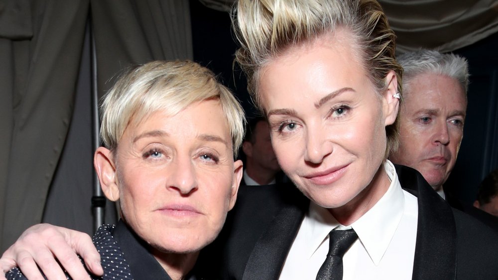 Ellen DeGeneres en un traje azul con lunares, Portia de Rossi con traje y corbata negra, posando con los brazos alrededor el uno del otro