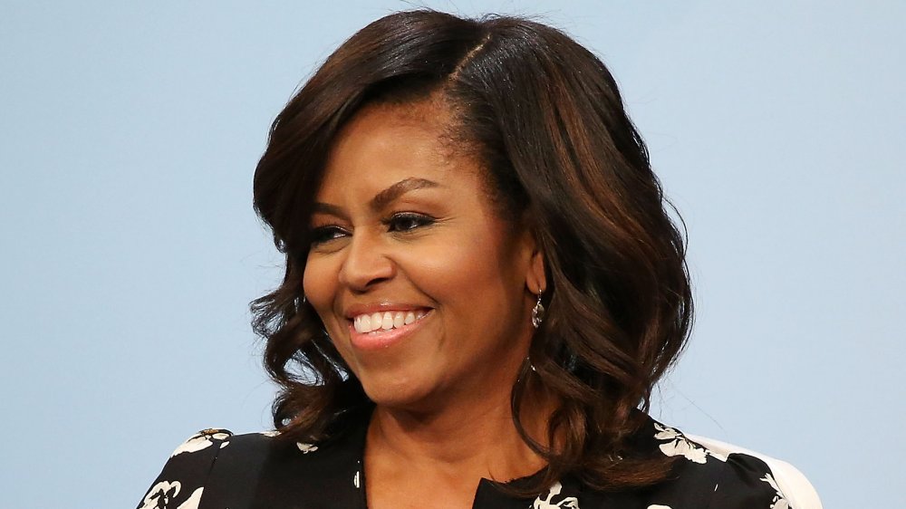 Michelle Obama con un vestido negro estampado floral, sonriendo mientras mira hacia un lado