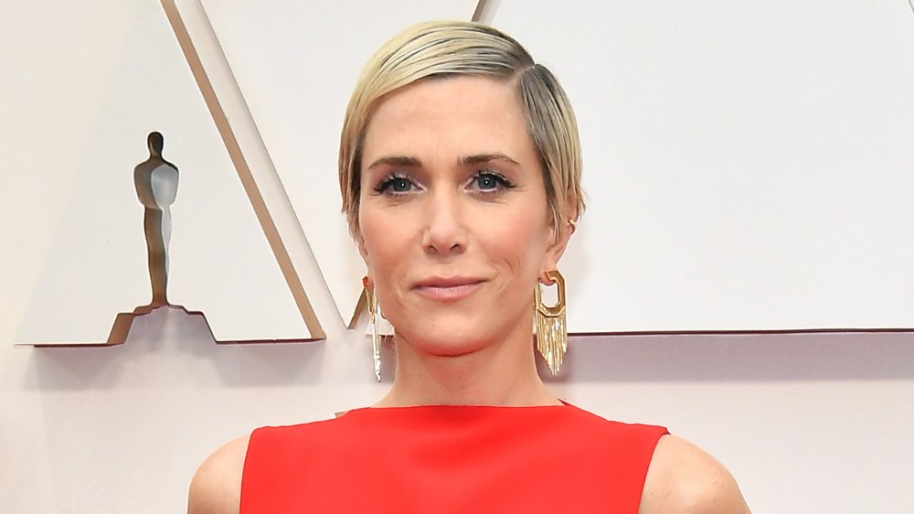 Kristen Wiig con un vestido rojo, sonriendo en la alfombra roja de los Oscar