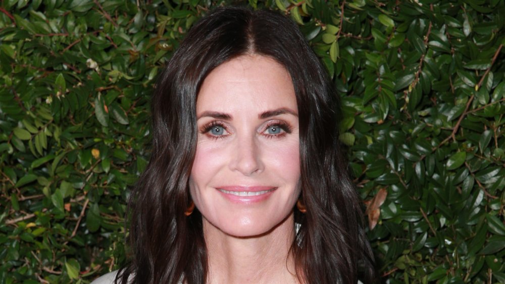 Courteney Cox con un vestido blanco y negro, sonriendo en un evento al aire libre