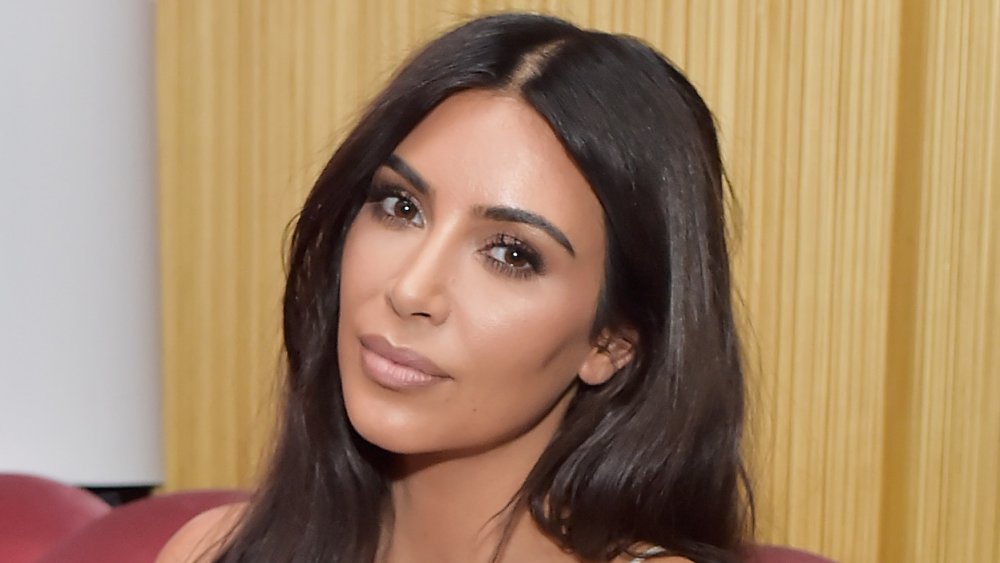 Kim Kardashian con un vestido blanco, posando en un sofá con la cabeza inclinada con una expresión neutra