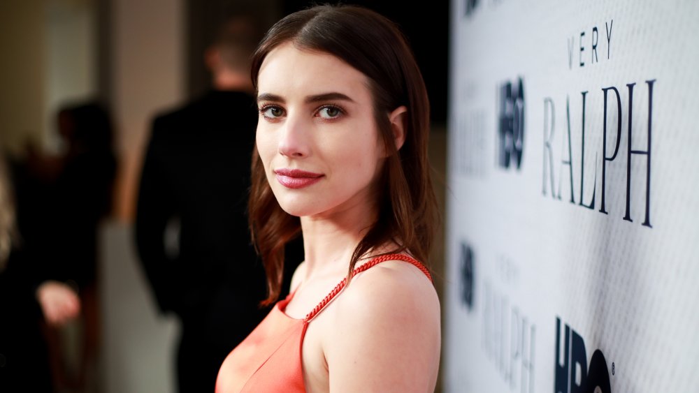 Emma Roberts con un vestido rojo con el pelo moreno, posando desde el lado en un paso y repetición