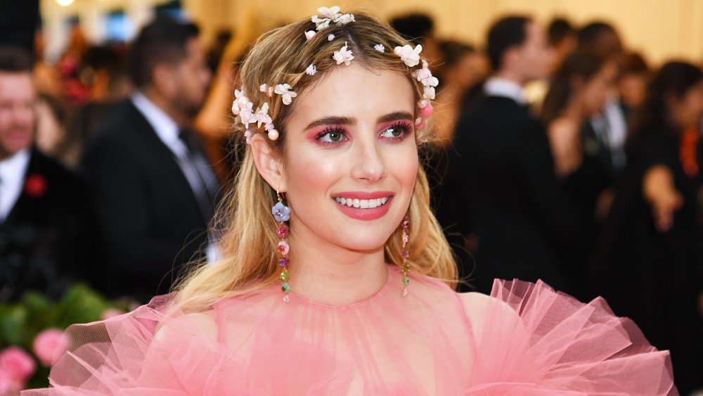 Emma Roberts con un vestido rosa y corona de flores, sonriendo