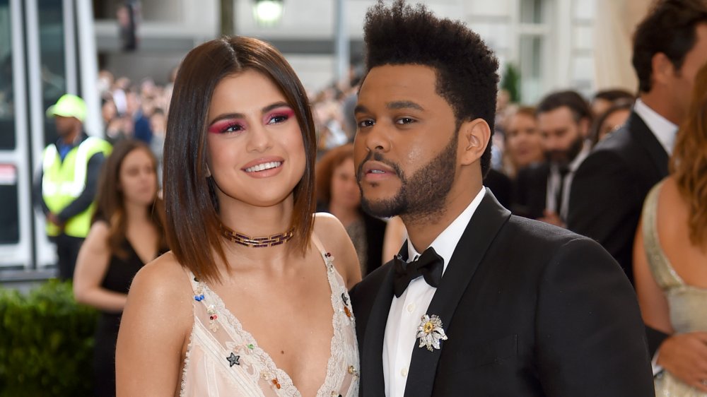 Selena Gomez con un vestido blanco, The Weeknd en traje negro