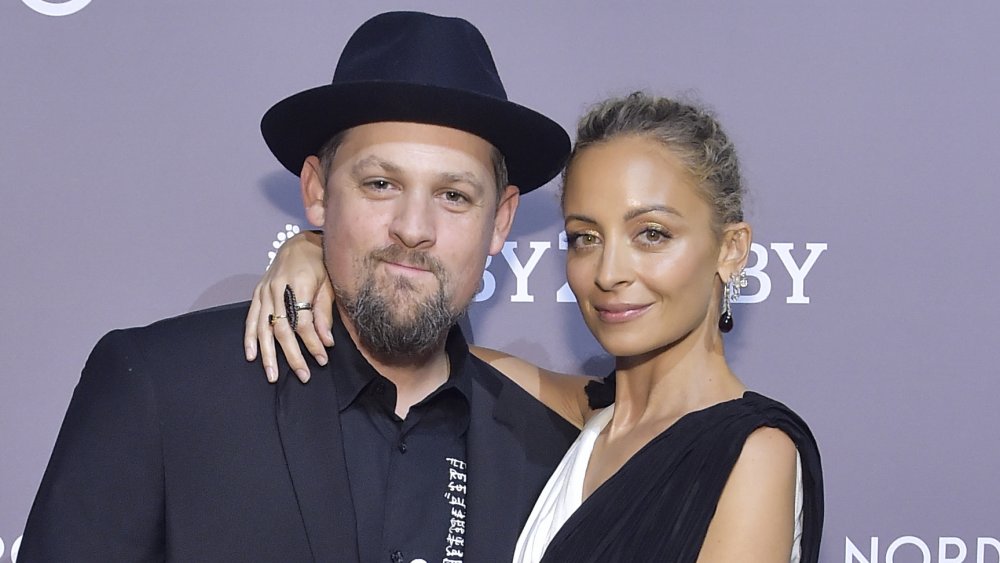 Joel Madden con traje y sombrero negros, Nicole Richie con un vestido blanco y negro, posando con los brazos alrededor y pequeñas sonrisas